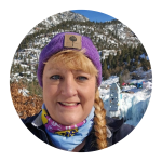 Woman with a purple beanie and braided hair smiles outdoors with a snowy mountain landscape, ready to discover the best food options in Colorado, from local favorites to unique dining experiences.