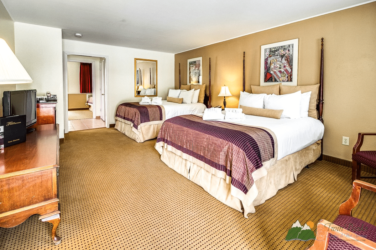 Spacious hotel room with two large beds, warm lighting, framed artwork, and classic wooden furniture.