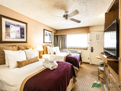 Cozy hotel room with two queen beds, ceiling fan, and flat-screen TV.