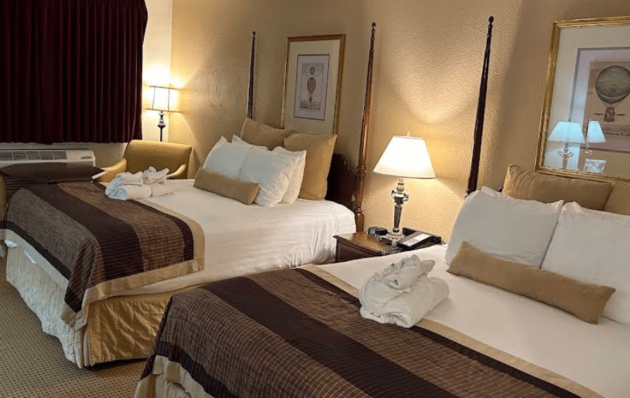 Warmly lit guest room with two four-poster beds and dark red curtains